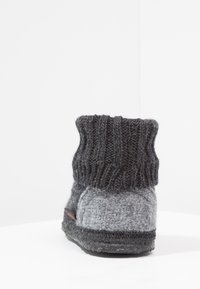 Gray felt slipper with a knitted dark gray cuff, rounded shape, low profile, and textured surface. Black rubber sole with red accent.