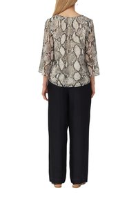 Haut léger et transparent avec un motif serpent et des manches trois-quarts ; assorti à un pantalon noir ample et des chaussures marron clair.