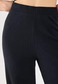 Pantalones anchos de canalé negros con cintura elástica suave y tejido texturizado, que resaltan líneas verticales a lo largo del material.