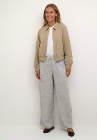 Beige cropped jacket with front pockets, paired with wide-leg striped pants in white and navy. Black flats complement the outfit.