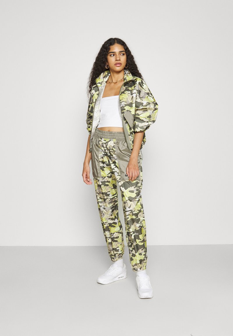 Chándal con estampado de camuflaje en tonos verdes y grises, con chaqueta corta y pantalones con cintura elástica, combinado con zapatillas blancas.