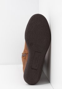 Chaussure en cuir marron avec semelle en caoutchouc texturée et léger talon. Fermeture éclair latérale et détails de couture subtils sur la tige.