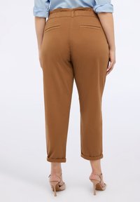 Pantaloni marroni a gamba affusolata con vita elasticizzata, due tasche posteriori e orli arrotolati. Indossati con sandali con tacco nudi.