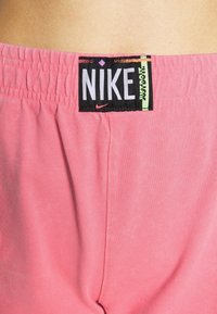 Rosa Nike-shorts med elastisk midja, med en svart etikett som visar logotypen och "JUST DO IT" i vit och grön text. Slät textur.