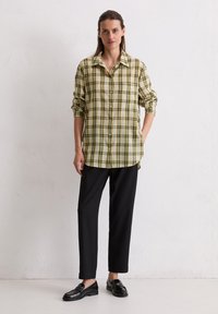 Oversized plaid shirt in green and yellow, button-up design with long sleeves, paired with black trousers and glossy black shoes.