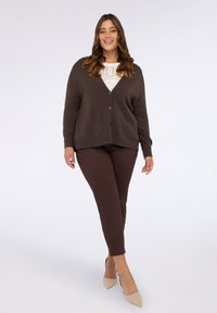 Brązowy kardigan zapinany na guziki, noszony na jasnym swetrze i zestawiony z brązowymi spodniami, dopełniony beżowymi szpilkami z noskiem w szpic.