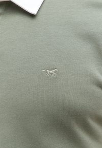 Koszulka polo z krótkim rękawem w jasnym zielonym kolorze, z białym kołnierzykiem i małym haftowanym logo konia na klatce piersiowej.