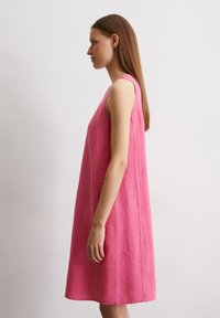 Ärmelloses A-Linien-Kleid aus leuchtend pinkem Leinen, mit einfachem Design und seitlichen Taschen, von der Seite gezeigt mit glatter Textur.