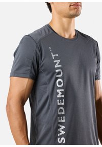 Harmaa urheilupaita lyhyillä hihoilla, jossa on itse asiassa pystysuuntainen "SWEDEMOUNT" -grafiikka vaaleanharmaana vasemmalla puolella. Sujuva, kevyt kangas.