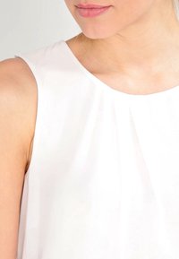 Top bianco senza maniche con scollatura rotonda, realizzato in tessuto morbido e liscio con una caduta leggera, che mette in evidenza una sottile lucentezza.
