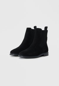 Stivali alla caviglia in suede nero con pannelli elastici sui lati, punta arrotondata e suola in gomma nera bassa. Design minimalista senza hardware visibile.