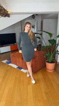 Grå stickad klänning med långa ärmar, figurnära form och ribbad struktur. Bärs med vita slip-on skor, i en modern interiör.