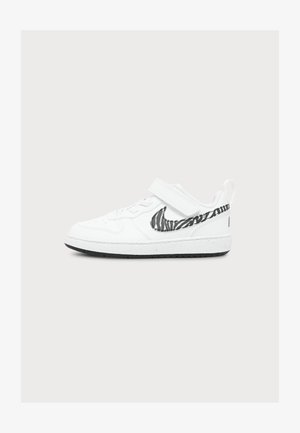 Baskets basses blanches avec un logo Nike motif zèbre noir et blanc et une fermeture à scratch sur un fond uni.