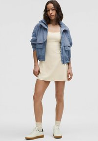 Vaaleansininen takki, beige istuva mekko, valkoiset tennarit, joissa on kumipohja, ja ribatutu kerma-sukat. Takissa on kaksi etutaskua ja huppu.