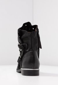 Black leather ankle boot with a textured finish, zip closure, star-shaped cutouts at the top, and a low stacked heel.