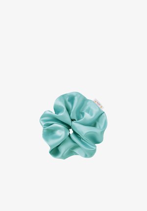 Turquoise satin scrunchie, featuring a smooth texture and gathered design, with a small label attached. Circular shape with a soft sheen.