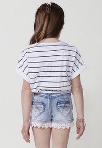 Top de manga corta a rayas blancas y azul marino, combinado con shorts de mezclilla azul claro que presentan bolsillos traseros en forma de corazón y un acabado de encaje en el dobladillo.