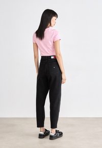 Rozā īsām piedurknēm T-krekls, melni augsta vidukļa tapas džinsi un melnas kurpes ar baltām akcentiem, skatīts no aizmugures.