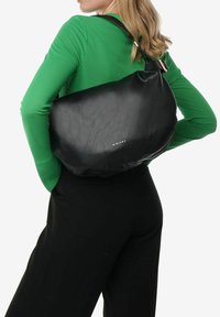 Sac à bandoulière en cuir noir avec une texture lisse, une forme courbée et une seule sangle. Présente un branding minimal et un design simple et élégant.