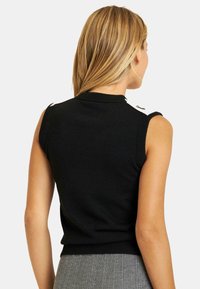 Top in maglia nera senza maniche con un colletto alto e dettagli sulle spalle, caratterizzato da una silhouette aderente e un orlo a coste.