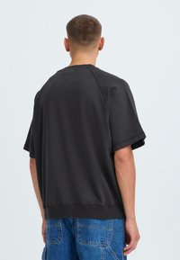 Felpa a maniche corte, di colore grigio scuro, realizzata in cotone. Presenta una vestibilità comoda e polsini a coste, con scollatura rotonda e una texture liscia.