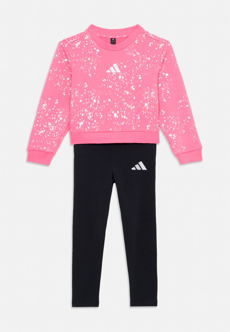 Felpa rosa con design a macchie bianche e logo Adidas, abbinata a leggings neri con logo bianco sulla gamba. Realizzata in materiale misto cotone.
