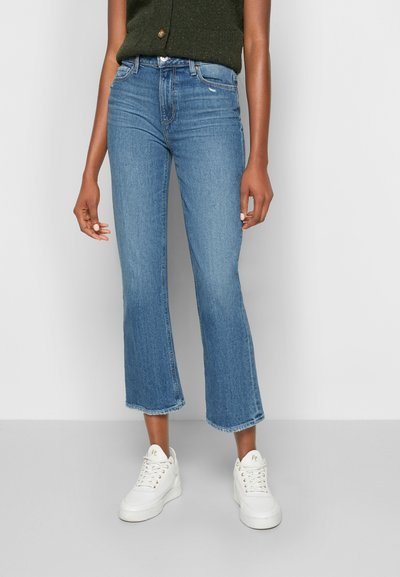 Jeans de denim azul claro com um design curto e amplo e bainha desgastada. Combinados com ténis brancos. Ajustados na cintura e anca.