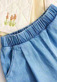 Lyseblå denimshorts med en samlet talje og sidelommer, parret med en hvid quilted stof med orange broderede blomster.
