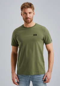 T-shirt a maniche corte verde oliva in cotone, con un collo rotondo e una piccola etichetta logo nera sul petto. Texture liscia.
