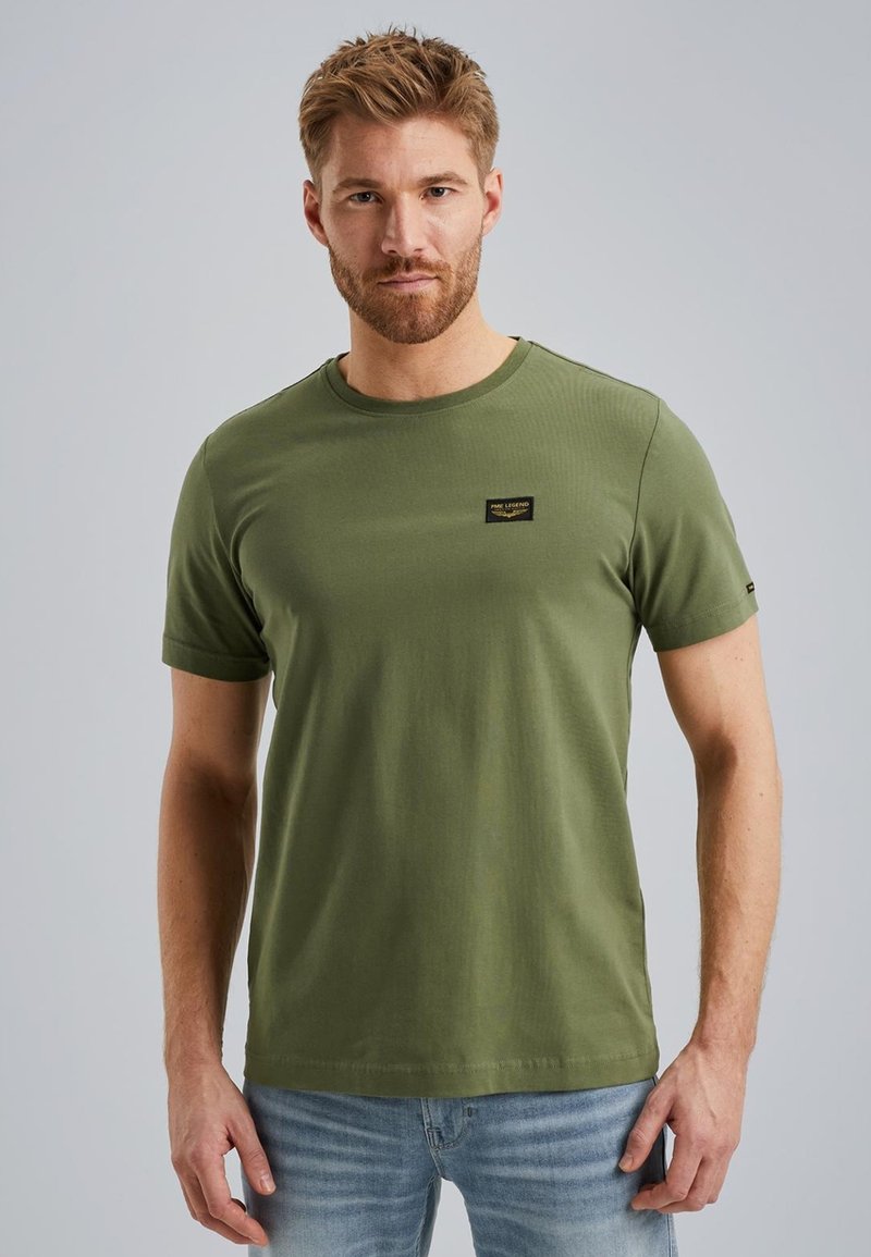 T-shirt a maniche corte verde oliva in cotone, con un collo rotondo e una piccola etichetta logo nera sul petto. Texture liscia.