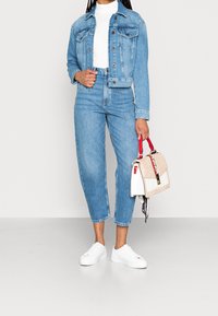 Ljust blå denimjacka med en kortad design, som matchas med högmidjade ljusblå jeans. Vita sneakers och en rosa och vit handväska med röda handtag.