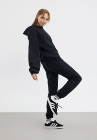 Svart huvtröja och sweatpants gjorda av mjukt tyg, tillsammans med svarta och vita sneakers. Har en oversized passform och ribbade mudd.