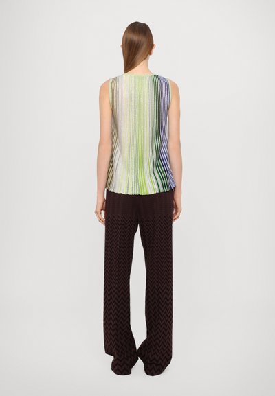 Top sin mangas metálico con rayas verticales multicolor; combinado con pantalones anchos marrones con un patrón de zigzag.