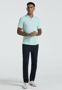 Mintgroene polo met een kraag, gecombineerd met marineblauwe cargobroeken. Witte sneakers met rode accenten. Glad materiaal met een klassieke pasvorm.