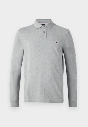 Polo de manga larga gris claro con una tapeta de dos botones y un pequeño logo rojo, blanco y azul en el lado izquierdo del pecho.