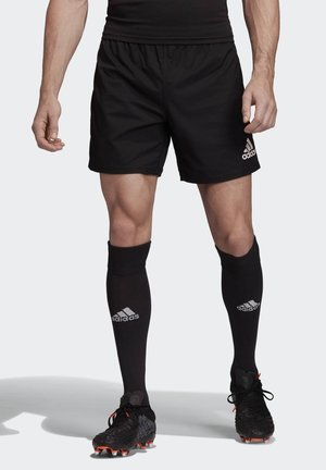 Zwarte sportshorts met een elastische tailleband, voorzien van een klein wit Adidas-logo. Gecombineerd met zwarte kniekousen en zwarte voetbalschoenen.