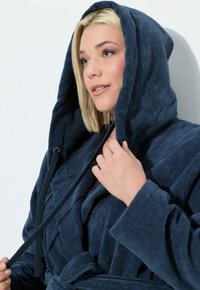 Accappatoio con cappuccio blu navy realizzato in morbido tessuto in spugna. Presenta una chiusura a legatura e un tessuto testurizzato con una vestibilità comoda, che mette in risalto un aspetto accogliente.