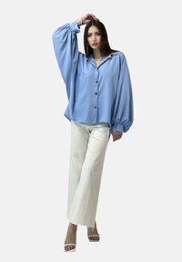Camisa de botones de gran tamaño de color azul claro con mangas amplias, botones en la parte delantera y cuello puntiagudo, combinada con pantalones anchos blancos.