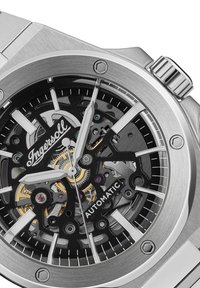 Automatisch horloge met een zilveren roestvrijstalen kast, zwart dial dat de mechanische beweging toont, zilveren wijzers en prominente markers.