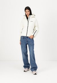 White hooded puffer jacket with a black zipper, paired with loose-fitting blue jeans and light pink sneakers. Smooth texture, minimal branding.