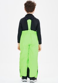 Pantaloni da sci impermeabili verdi con spalline regolabili e cerniere laterali, indossati sopra una maglietta nera, dotati di vita elastica per il massimo comfort.