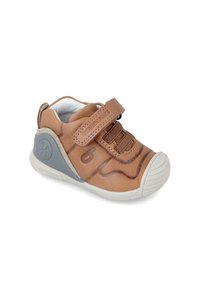 Zapato de cuero marrón con una correa de velcro, acentos grises texturizados, punta redondeada de goma y un forro suave. Presenta un logo en el lateral.