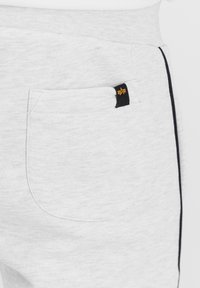 Svetlo sivi joggerji z teksturirano površino, z zadnjim žepom in črnimi stranskimi črtami. Vsebujejo majhno črno oznako z zlatim detajlom.