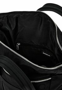 Intérieur d'un sac noir avec un tissu lisse. Comprend une poche centrale zippée et une étiquette intérieure, soulignée par une fermeture éclair argentée le long de l'ouverture.