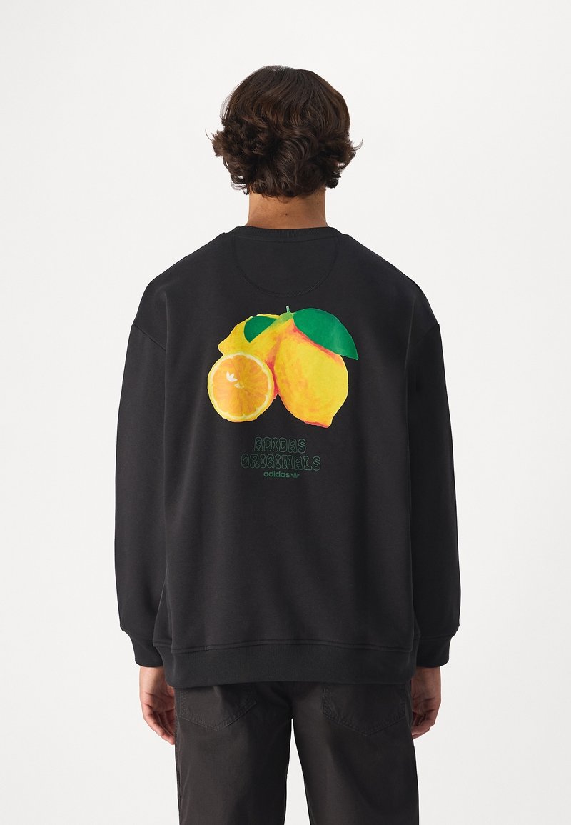 Schwarzer Sweatshirt mit einem bunten Grafik von Zitrone und Orange auf dem Rücken, darüber grüner Text mit der Aufschrift "Adidas Originals".