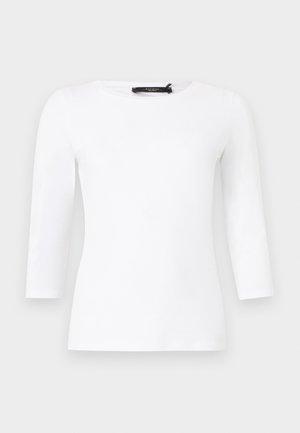 Λευκό μακρυμάνικο εφαρμοστό μπλουζάκι με στρογγυλή λαιμόκοψη και εμφανές μαύρο ετικετάκι επωνυμίας στο λαιμό, σε απλό φόντο.