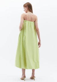 Grünes trägerloses Kleid aus einem fließenden Stoff, knielang, mit gerafftem Rücken, kombiniert mit goldenen Absatzsandalen.