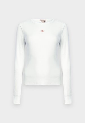 Weißes, geripptes Langarmshirt mit kleinem rechteckigem Calvin Klein Logo-Patch, zentriert unterhalb des Halsausschnitts.