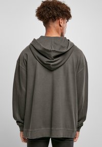 Oversized grå hettegenser med en myk tekstur, med en stor hette, senkede skuldre og ribbestrikkede mansjetter og kant. Baksidevinkelen vist.