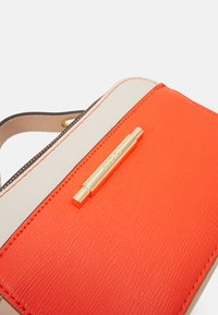 Borsa colorata con una parte anteriore in pelle arancione brillante, retro beige, hardware dorato e una finitura testurizzata con dettagli di cucitura prominenti.